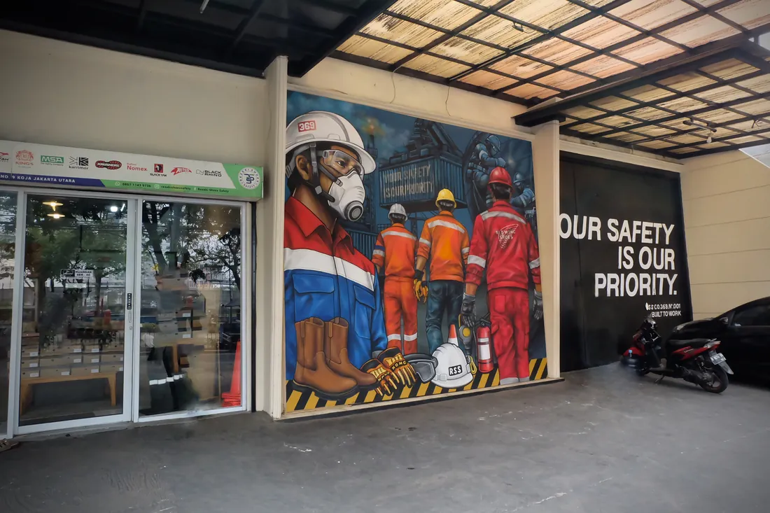 Pintu masuk toko dan mural pekerja safety bertuliskan Our Safety Is Our Priority